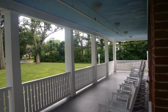 Covered porch with white rocking chairs overlooking a leafy lawn.