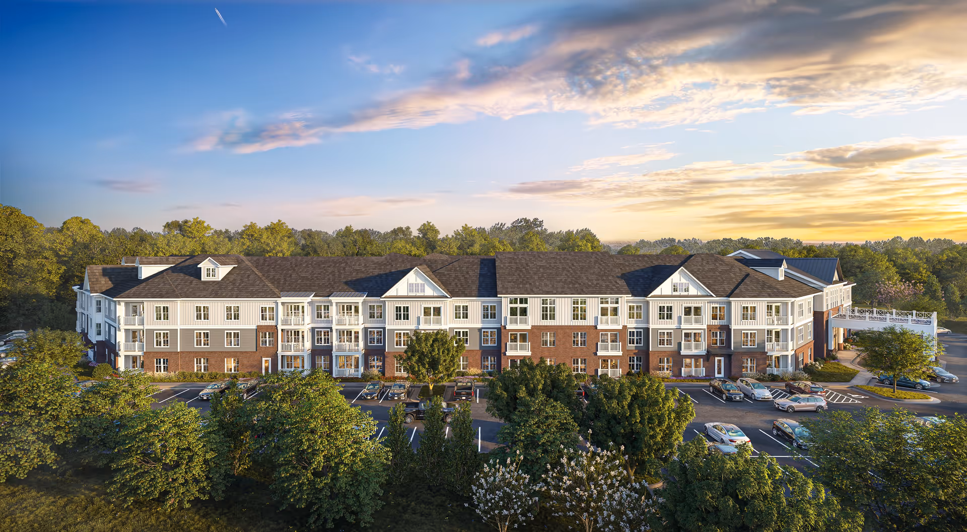 Exterior view of a large, multi-story senior living facility building named Lake Forest at Swift Creek, surrounded by trees and a parking lot with cars, under a partly cloudy sky at sunset.