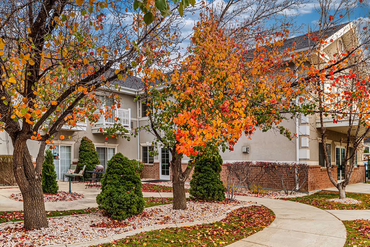 Courtyard and walkway in front of a senior living building with colorful autumn trees and landscaping.