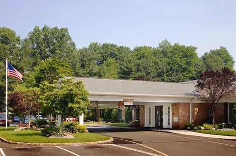Senior living facility entrance with a covered drop-off, flag, and well-kept landscaping.