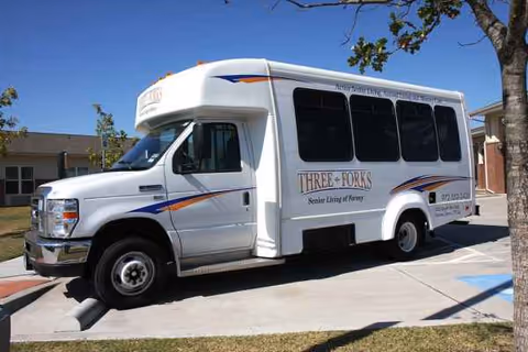 White shuttle bus with colorful stripes parked outside a senior living facility.