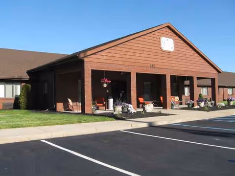 Oakbrook Village building entrance with brick exterior, porch seating, and potted plants.