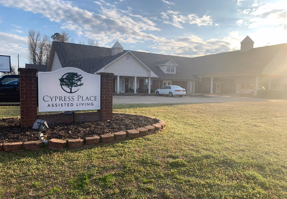 A Cypress Place Assisted Living sign in front of the facility building and grassy lawn under a sunny sky.