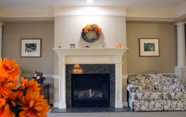 Cozy common living room with a lit fireplace, wreath-decorated mantel, floral sofa and orange flowers in the foreground.
