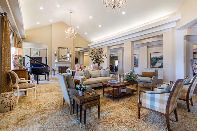 Spacious, elegantly furnished communal living room with sofas, armchairs, chandeliers, coffee tables, and a grand piano.