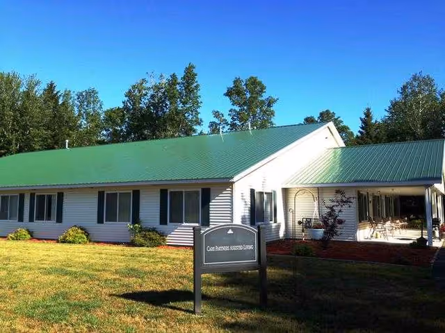 Single-story white senior living facility front view with a green roof and lawn.