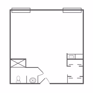 A simple architectural floor plan showing a rectangular room with a small bathroom area in the bottom left corner, including a toilet and sink. There are two windows on the top wall and a small kitchenette or closet area on the right side.