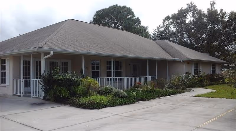 Single-story beige building with a covered porch and white railing, landscaped front beds and a paved driveway.