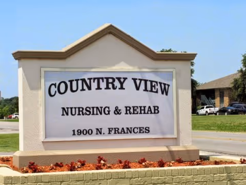 Outdoor sign for Country View Nursing & Rehab located at 1900 N. Frances, set on a landscaped base with red mulch and small plants, with a road and some buildings and cars in the background.