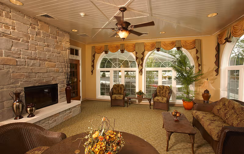Comfortable common room with a stone fireplace, wicker sofas and armchairs facing large arched windows.