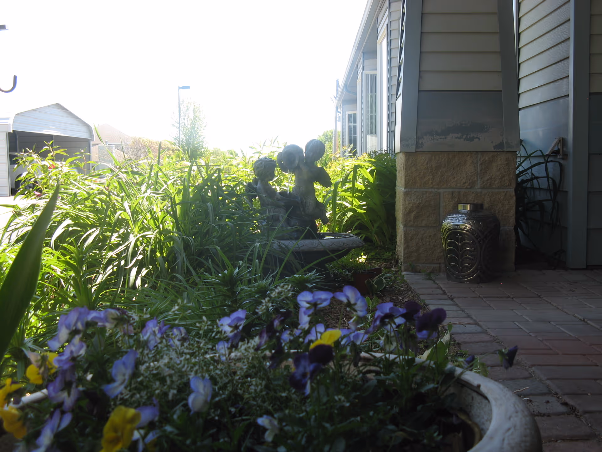 Potted flowers and greenery framing a small cherub fountain next to a building's exterior walkway.