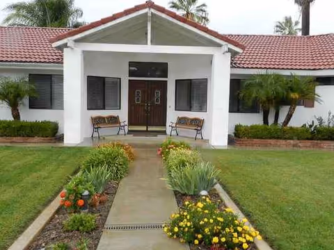 Front view of Meadowbrook Homes facility with a walkway, benches, and landscaped flower beds.