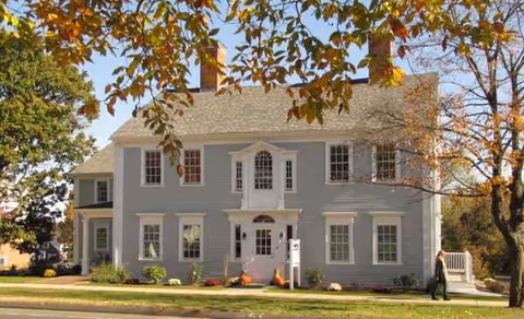 Two-story gray-blue building with white trim and autumn foliage framing the front entrance.