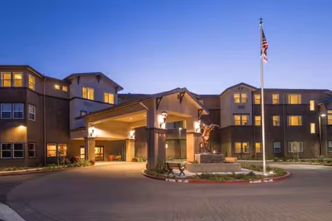 Exterior view of Carlton Senior Living Davis entrance with porte-cochère and American flag at dusk