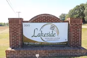A brick sign for Lakeside Senior Living Community with the address number 390, phone number 731-352-4567, and website www.lakesidesenior.com, set outdoors with trees and a clear sky in the background.