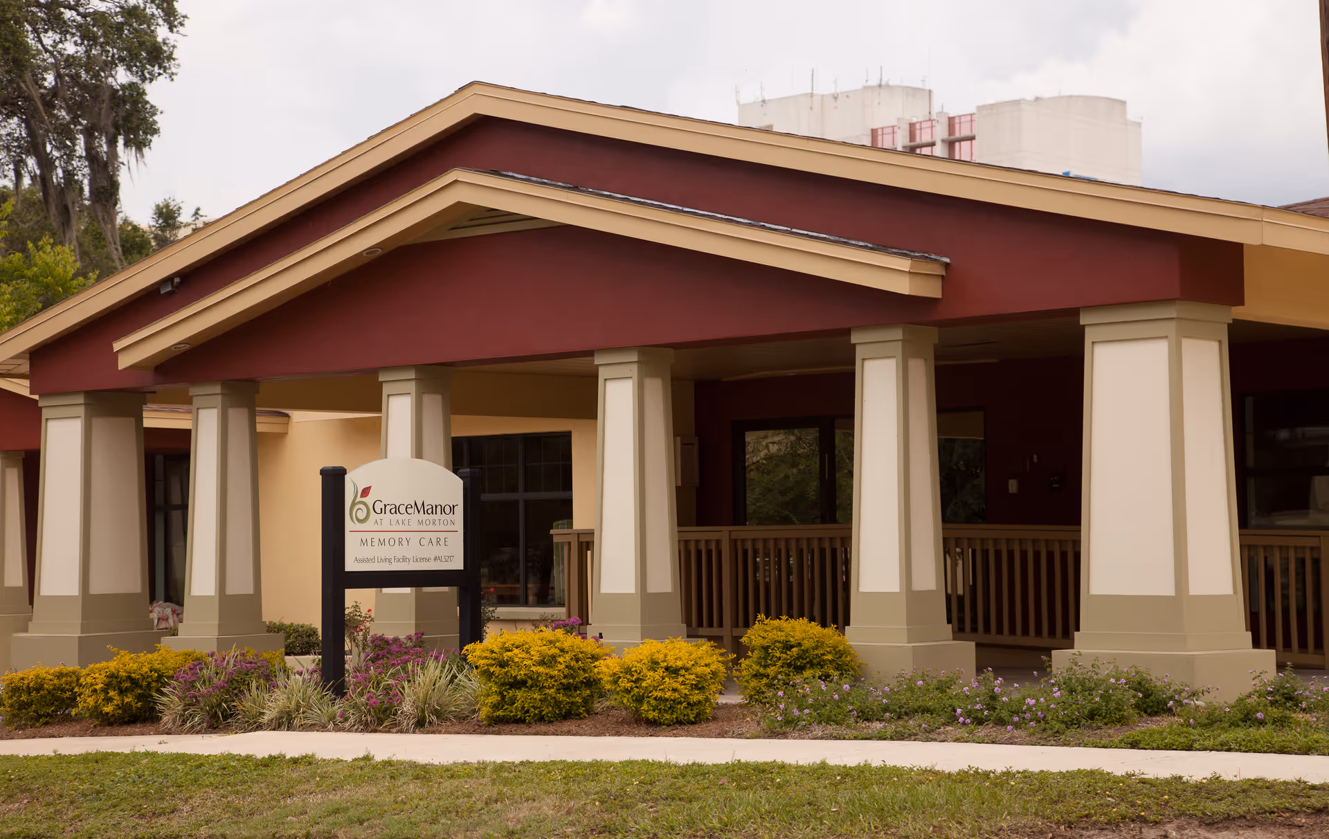 Entrance of Grace Manor at Lake Morton memory care facility with a covered porch, columns, sign, and landscaped shrubs.