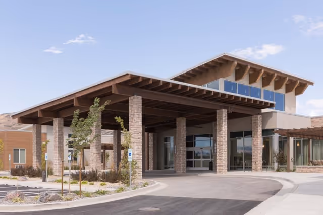 Front exterior entrance of a senior living building with a large covered porte-cochere supported by stone columns and a circular driveway.