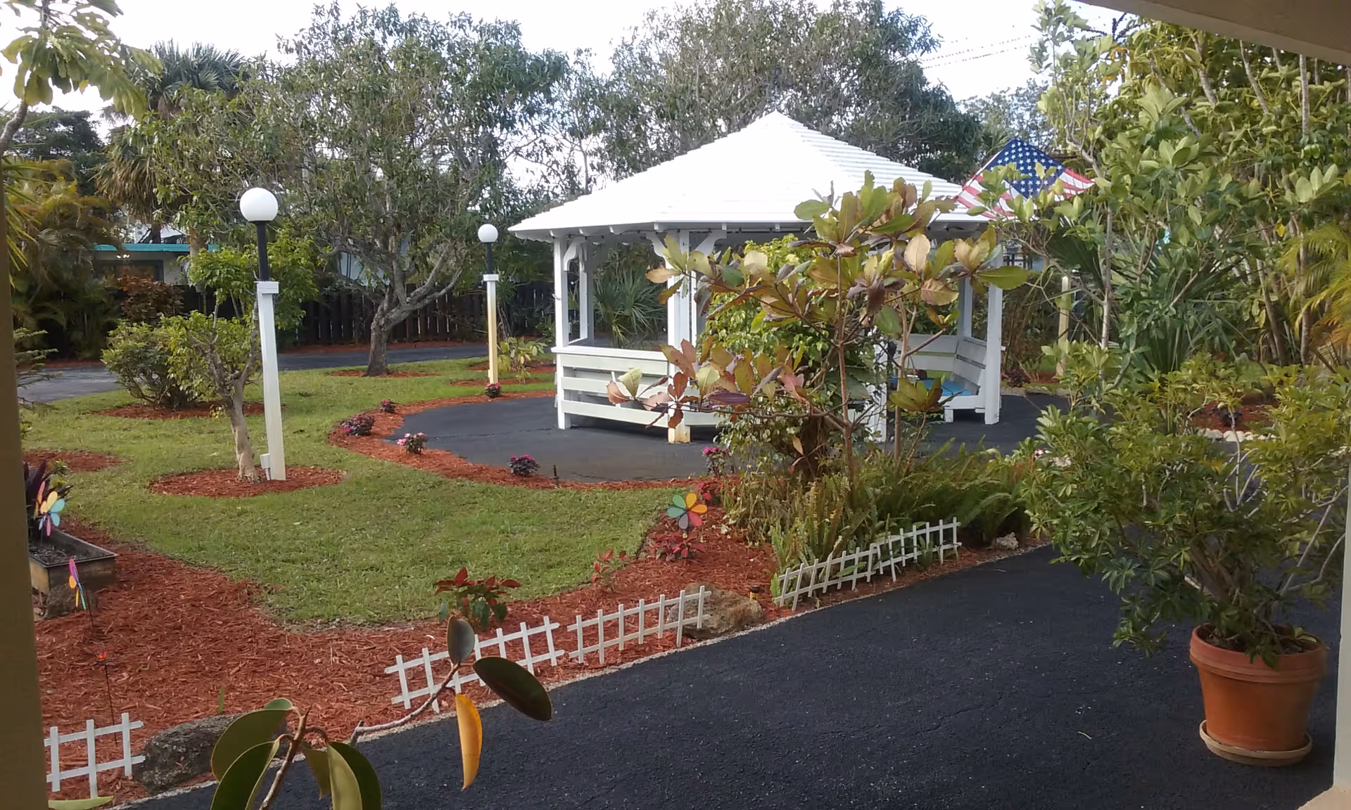 A landscaped courtyard with a white gazebo, walking paths, lamp posts, and potted plants.