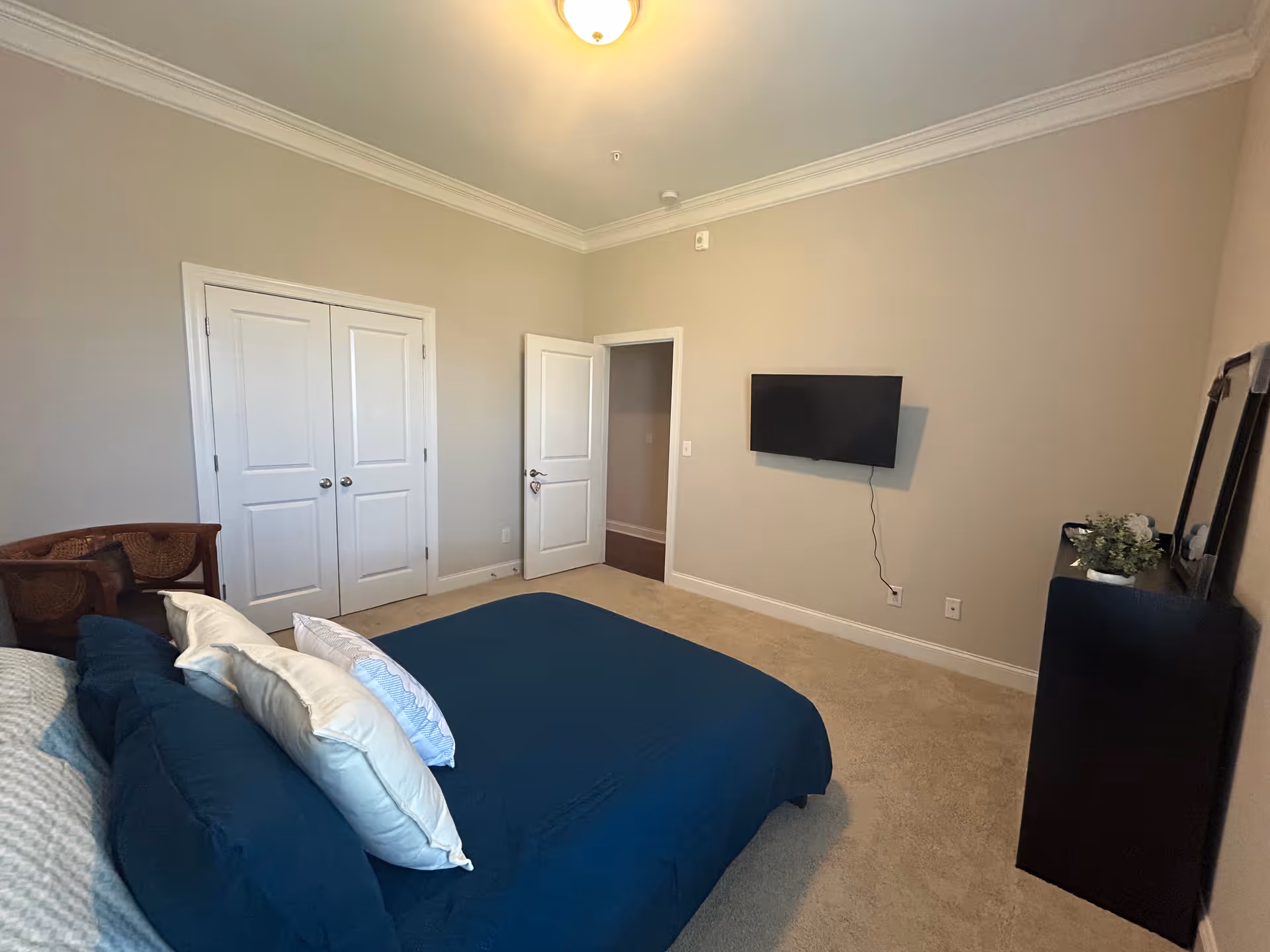 Bedroom with a blue-covered bed and pillows, a wall-mounted TV, double closet doors, and a dresser against neutral-colored walls.