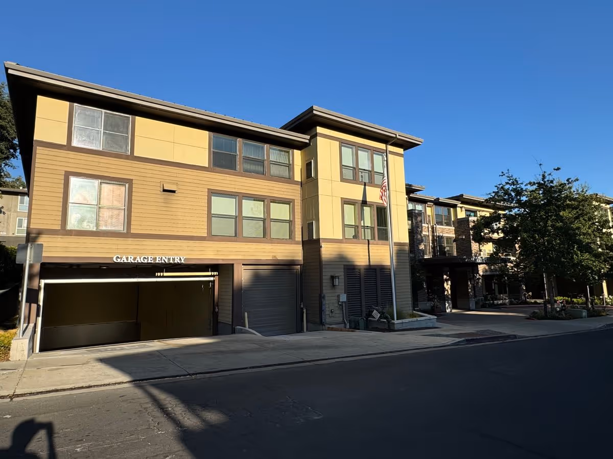 Front exterior of a multi-story residential building with a garage entry, windows, and an American flag.