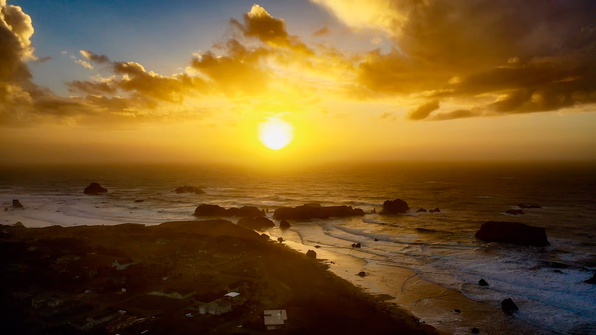 Aerial view of a rocky coastline and ocean bathed in golden light from a setting sun.