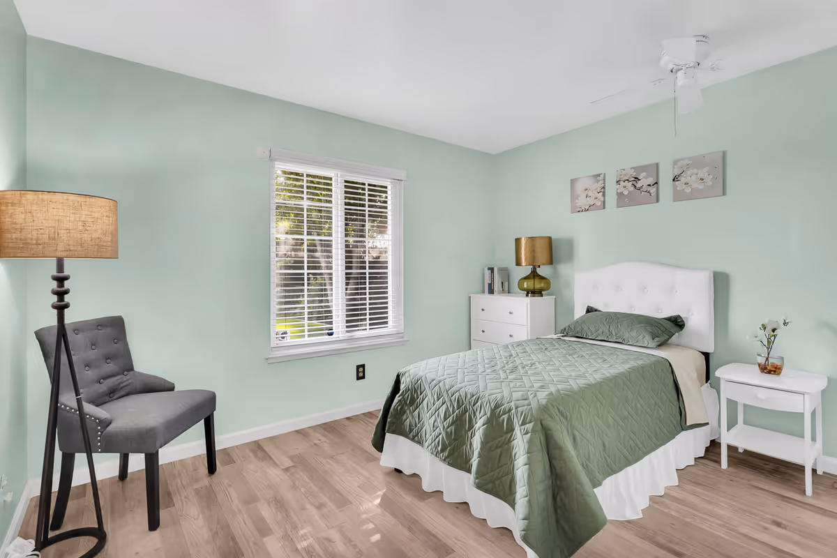 Mint-green bedroom with a white bed, dresser, nightstand, lamp, and window.