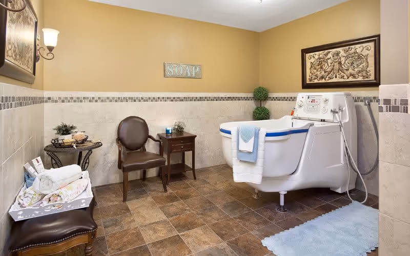A well-designed bathroom featuring a large bathtub, a wooden chair, and decorative elements like a framed artwork and a 'SOAP' sign on the wall.