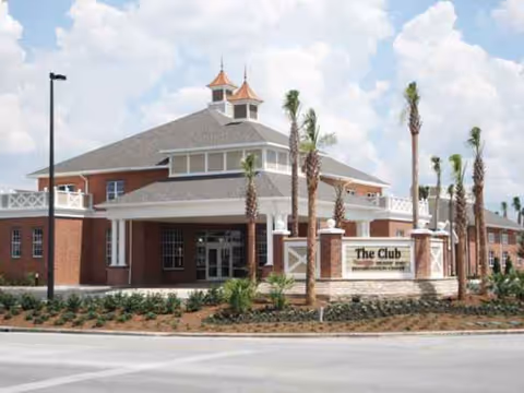 Front exterior of a brick senior living facility with palm trees and a sign.