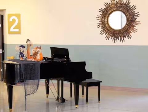 A glossy black grand piano sits in a light, airy lobby with a sunburst mirror.