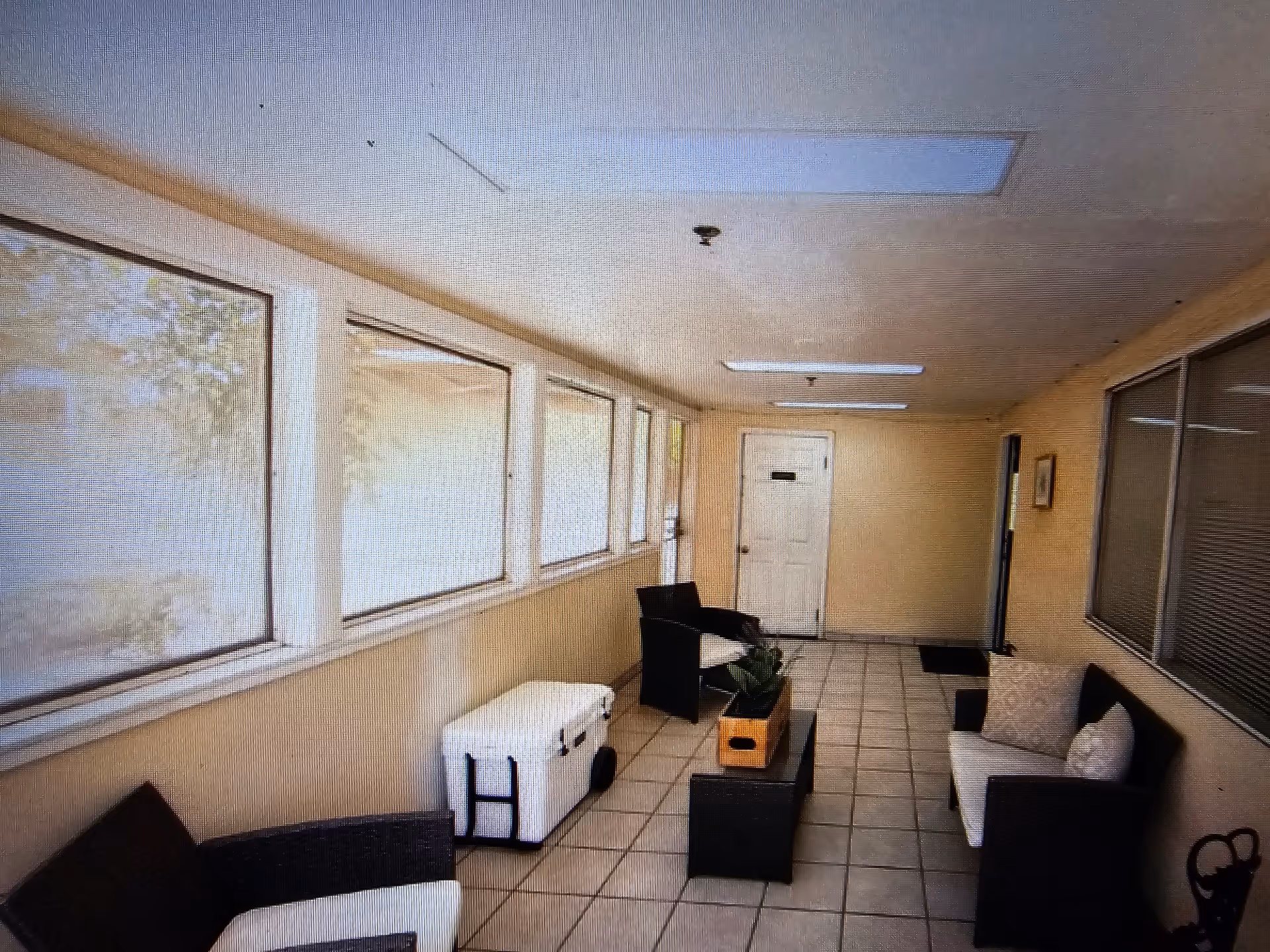 Enclosed sunroom-style seating area with tile floor, wicker chairs, small tables and large windows along one wall.