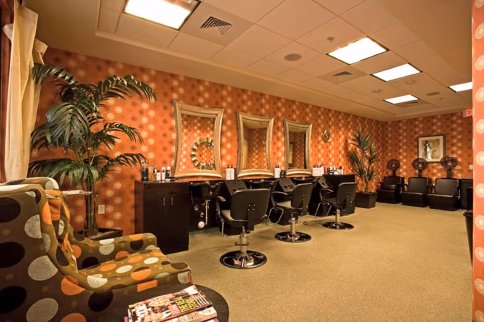 Interior salon with styling chairs, mirrors and hair-drying stations against patterned orange wallpaper.