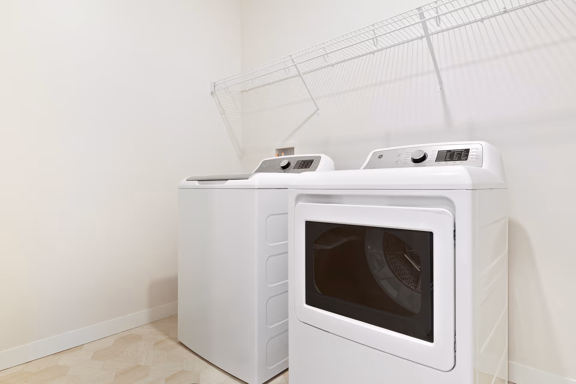 Laundry room with a white top-loading washer and front-loading dryer beneath a wire shelf.
