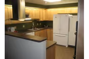 Bright, compact kitchen with wooden cabinets, refrigerator, sink, and breakfast bar.