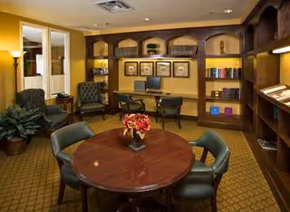 Cozy lounge area in a senior living facility with a round table, chairs, and bookshelves.