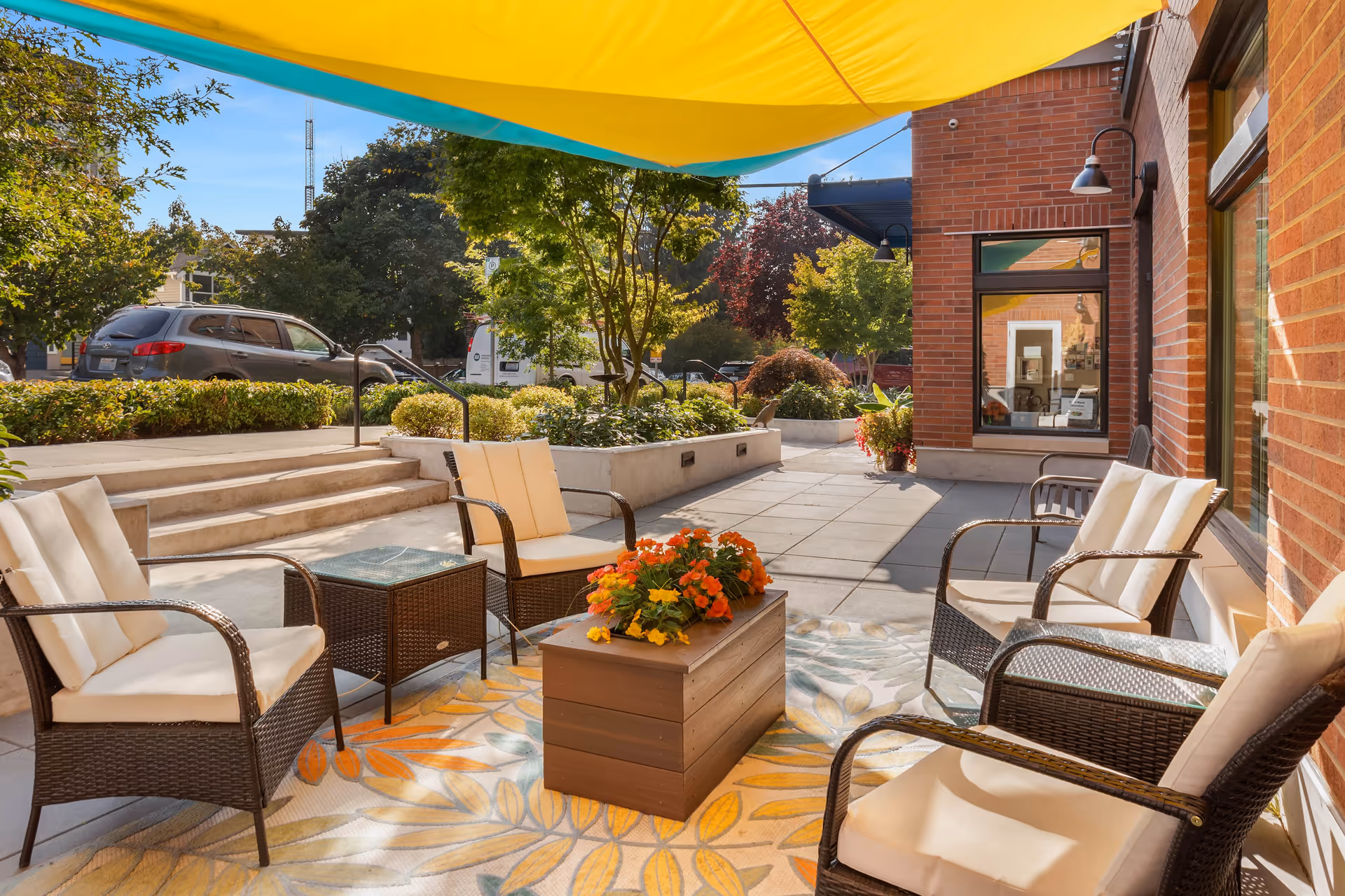 Outdoor seating area with chairs and a table under colorful awnings surrounded by plants.