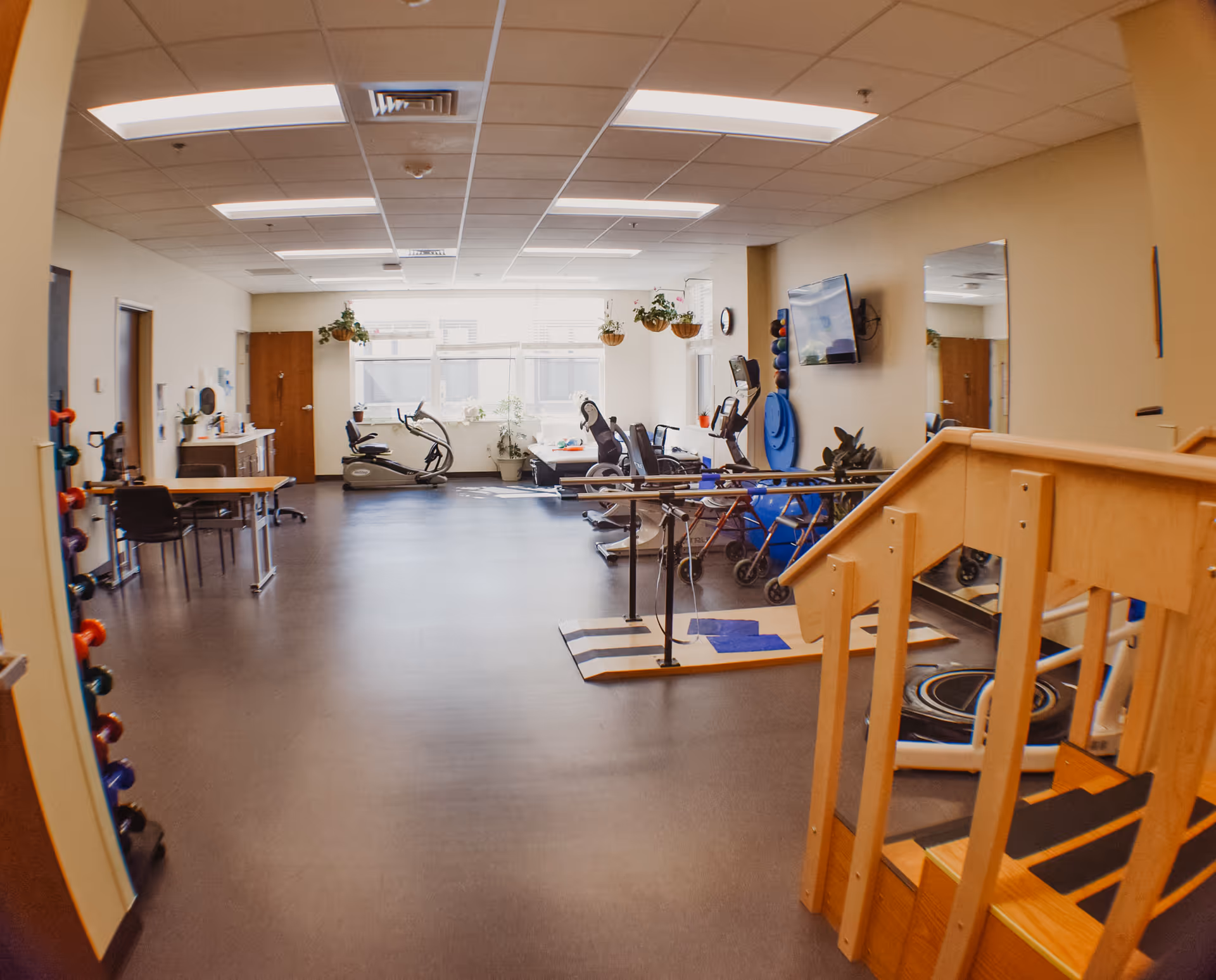 Exercise and rehabilitation room with parallel bars, stationary bikes, therapy stairs, and weights.