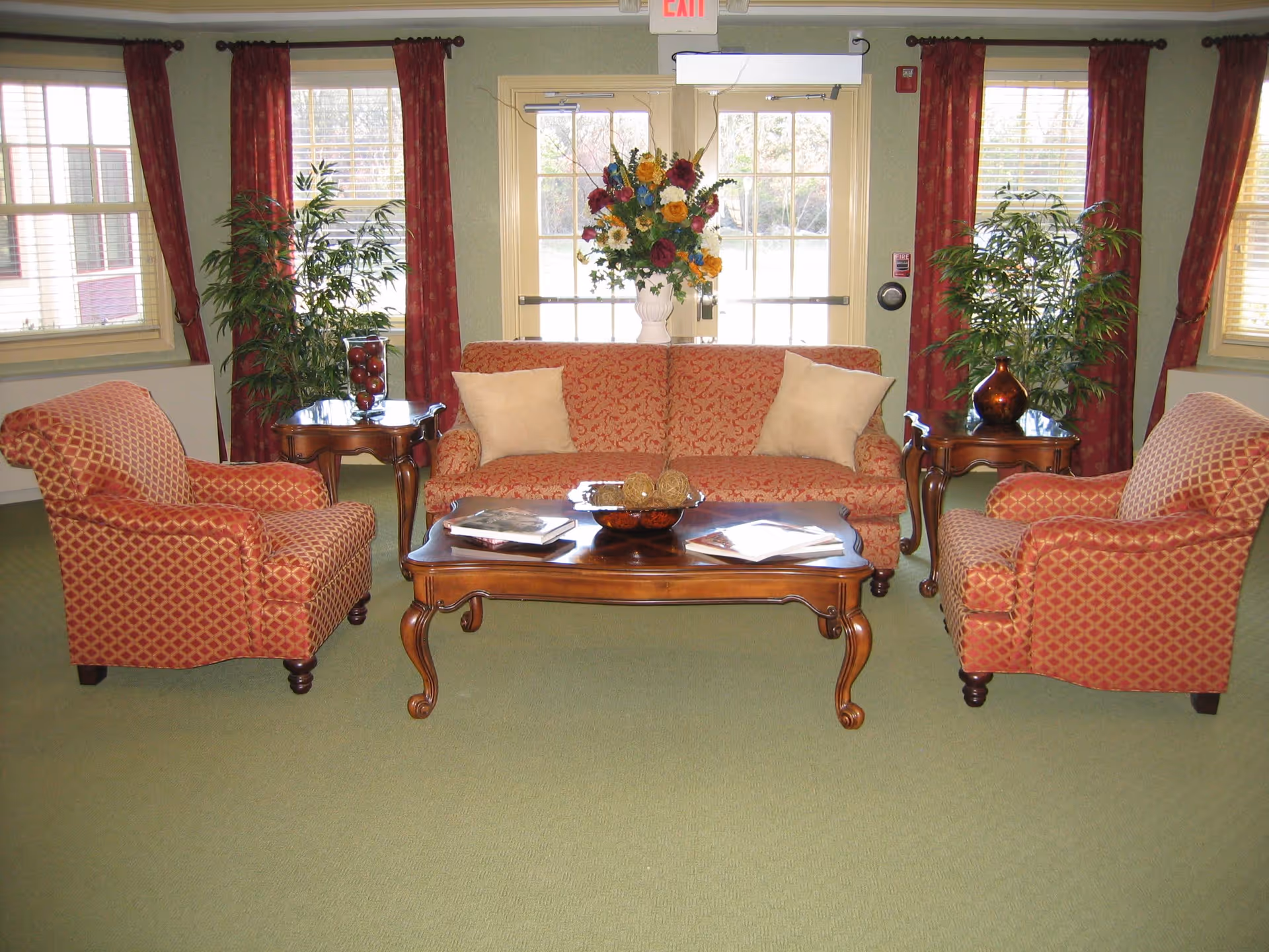 Cozy sitting area with patterned sofa and two armchairs around a wooden coffee table in a well-lit common room.