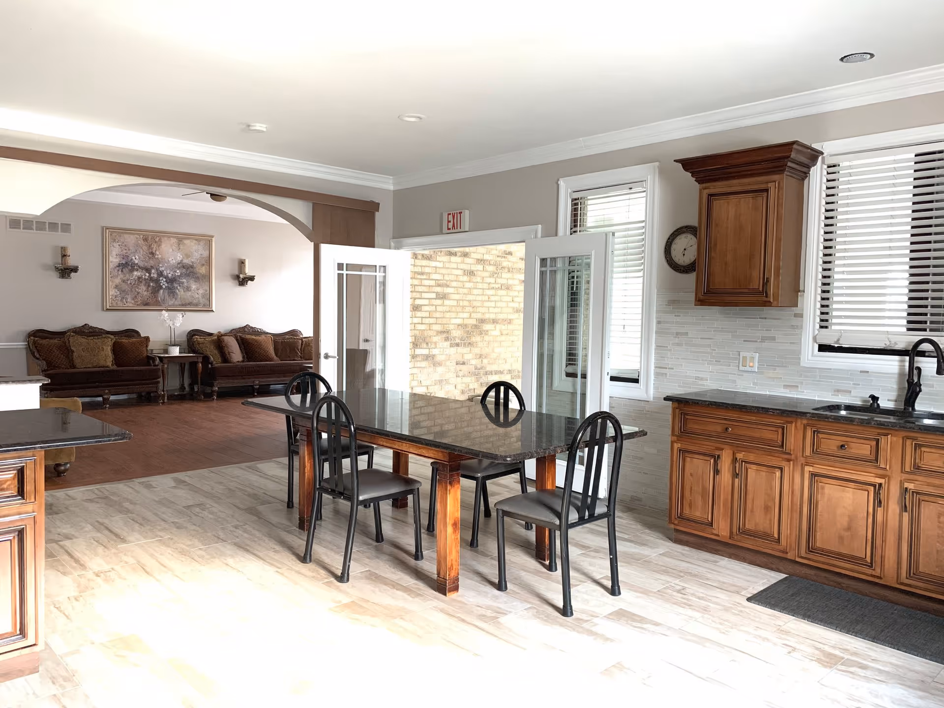 Open-plan dining area and kitchen with a dark dining table and four chairs, wooden cabinets, and a seating area visible in the background.