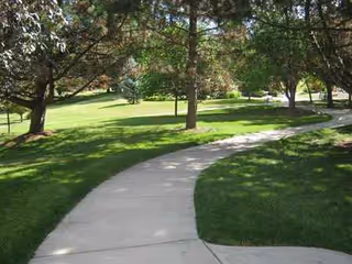 Curved concrete sidewalk winds through a green, tree-filled outdoor area at Sanctuary at St Paul's.