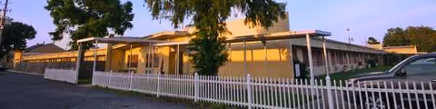 Exterior view of Waldon Health Care Center with white fence and parked cars.