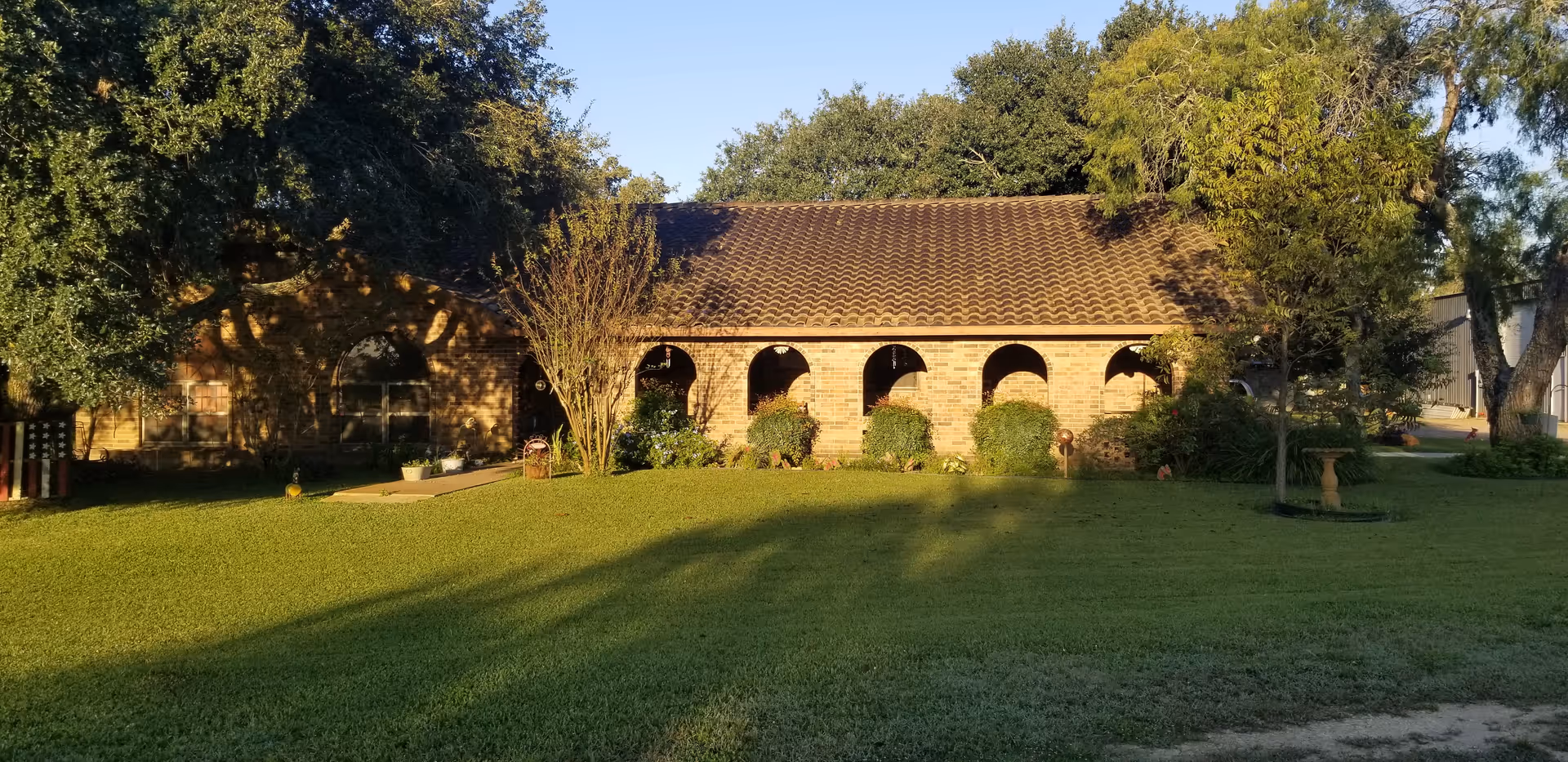 Single-story brick building with a tiled roof and arched front porch set behind a lawn and trees.