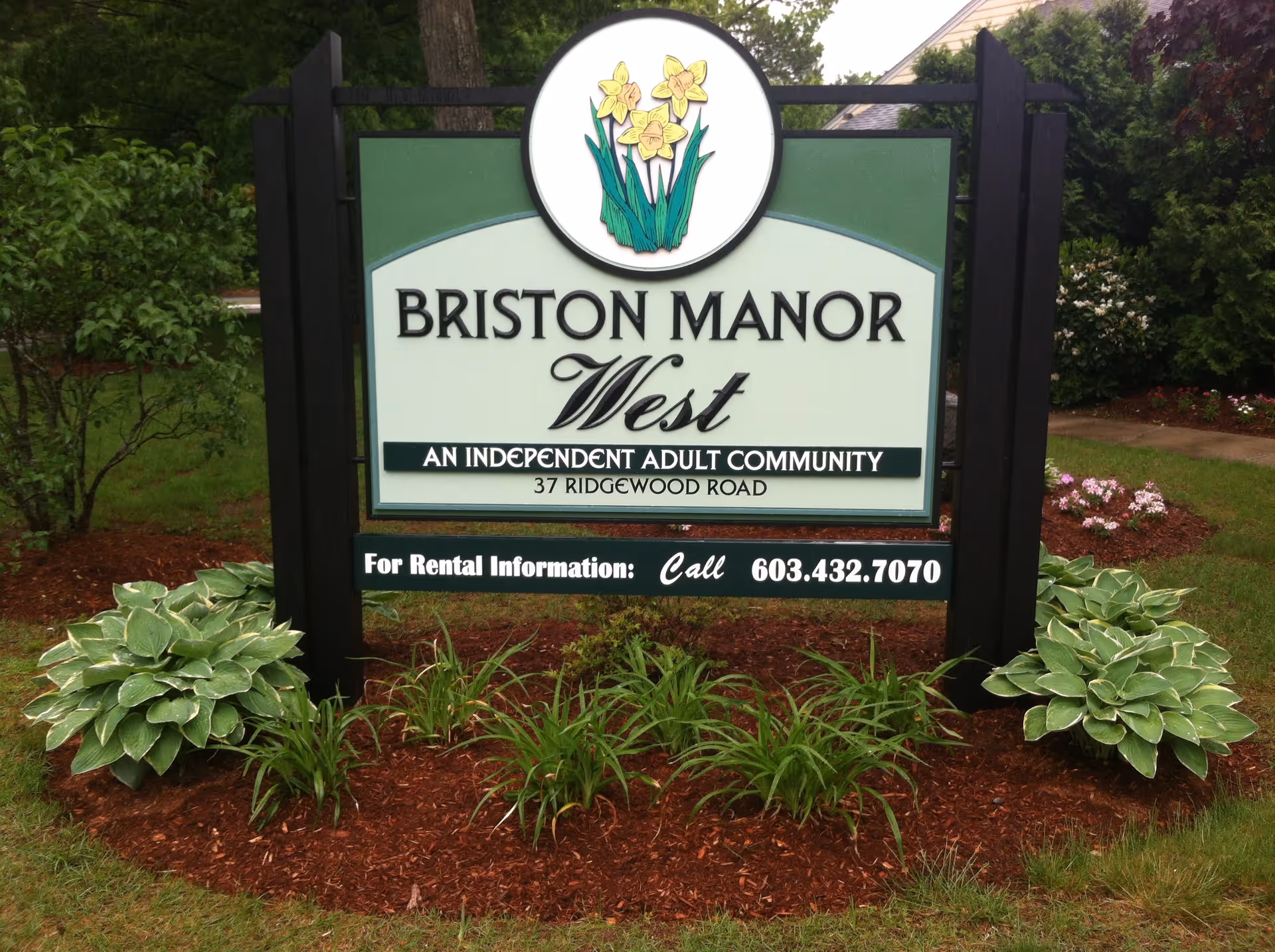 Outdoor sign for Briston Manor West, an independent adult community located at 37 Ridgewood Road, surrounded by green plants and mulch.