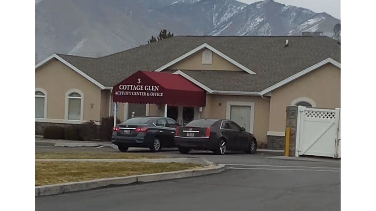 Exterior view of Cottage Glen Assisted Living with a maroon entrance canopy and parked cars in front.