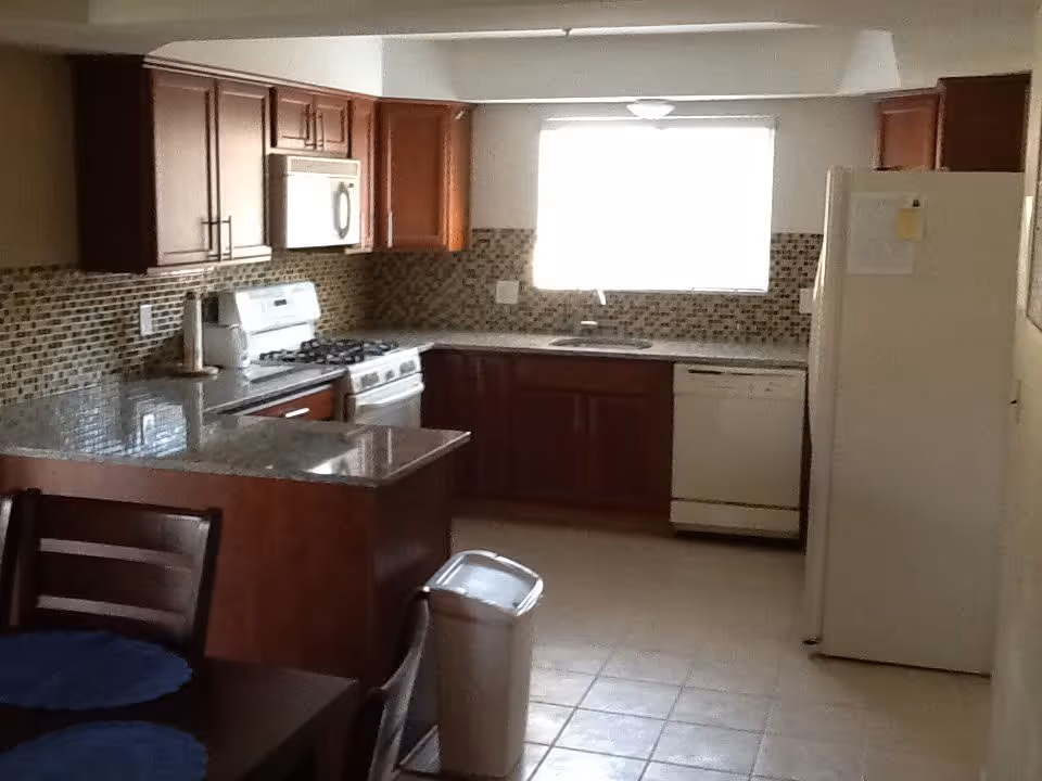 Kitchen with wooden cabinets, tiled backsplash, gas stove, refrigerator, dishwasher, and a small dining table.