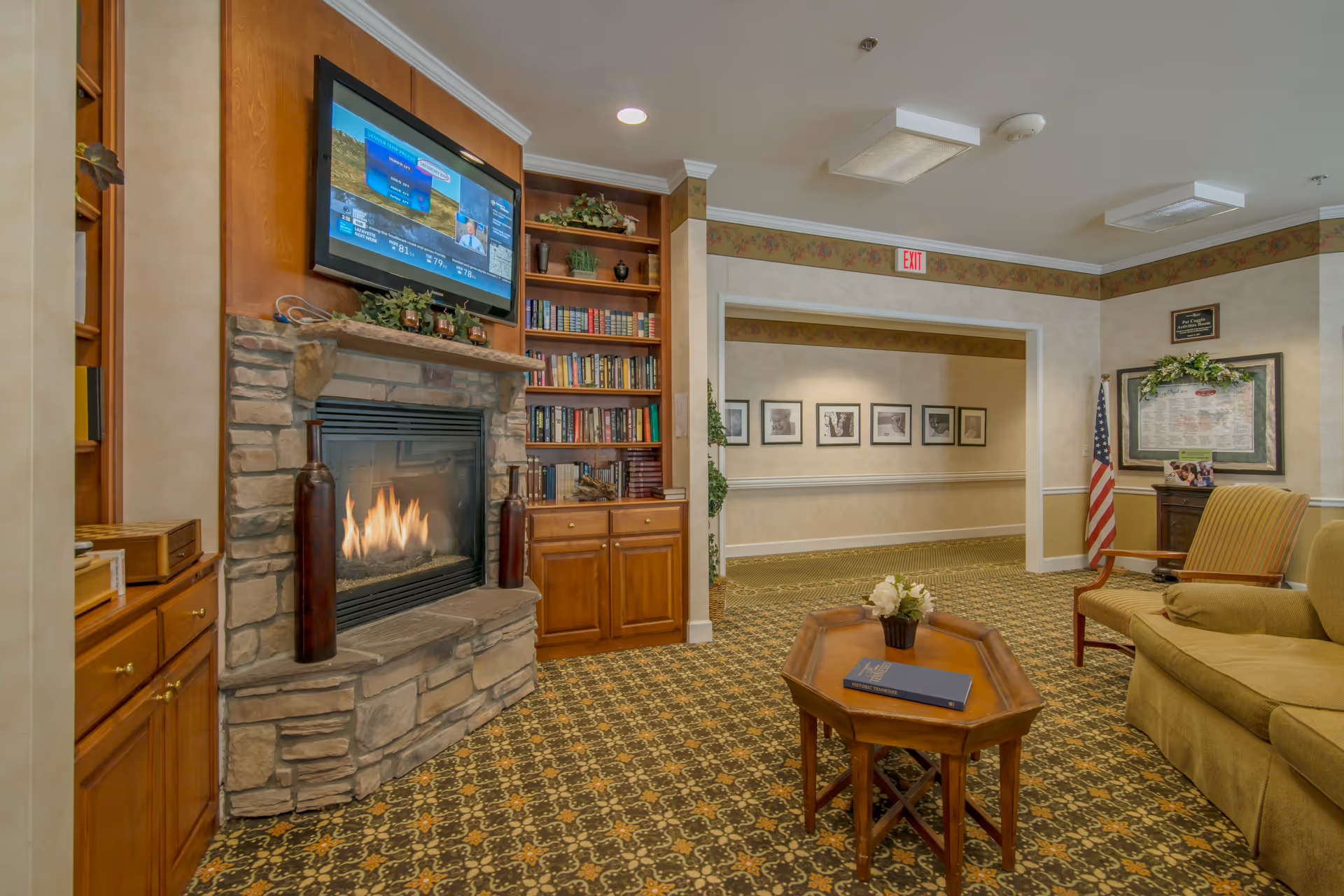 Cozy common room with a stone fireplace, built-in bookshelves, a wall-mounted TV, seating and a coffee table.