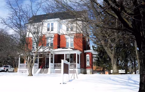 Two-story red-brick Getman Memorial Home with white trim and a snow-covered front yard.