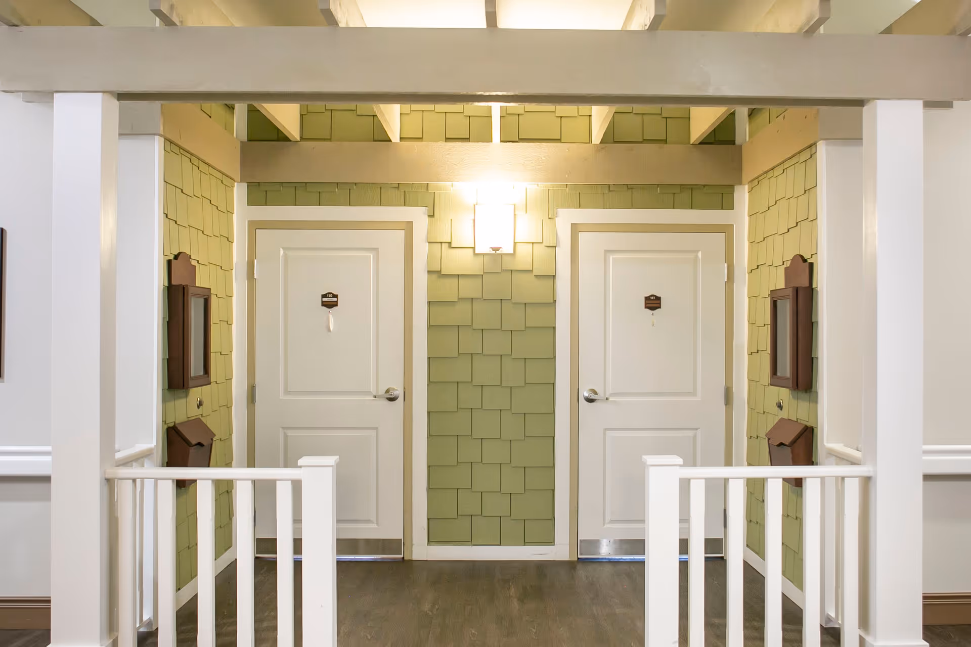 Interior hallway styled like a small porch with two white doors set in light green shingled walls and white railings.