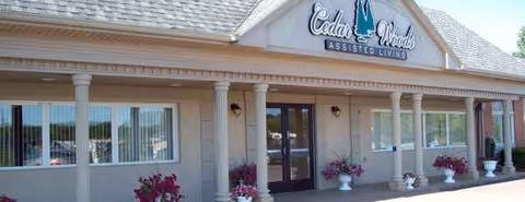 Front view of CedarWoods Assisted Living facility with entrance, columns, and potted flowers.