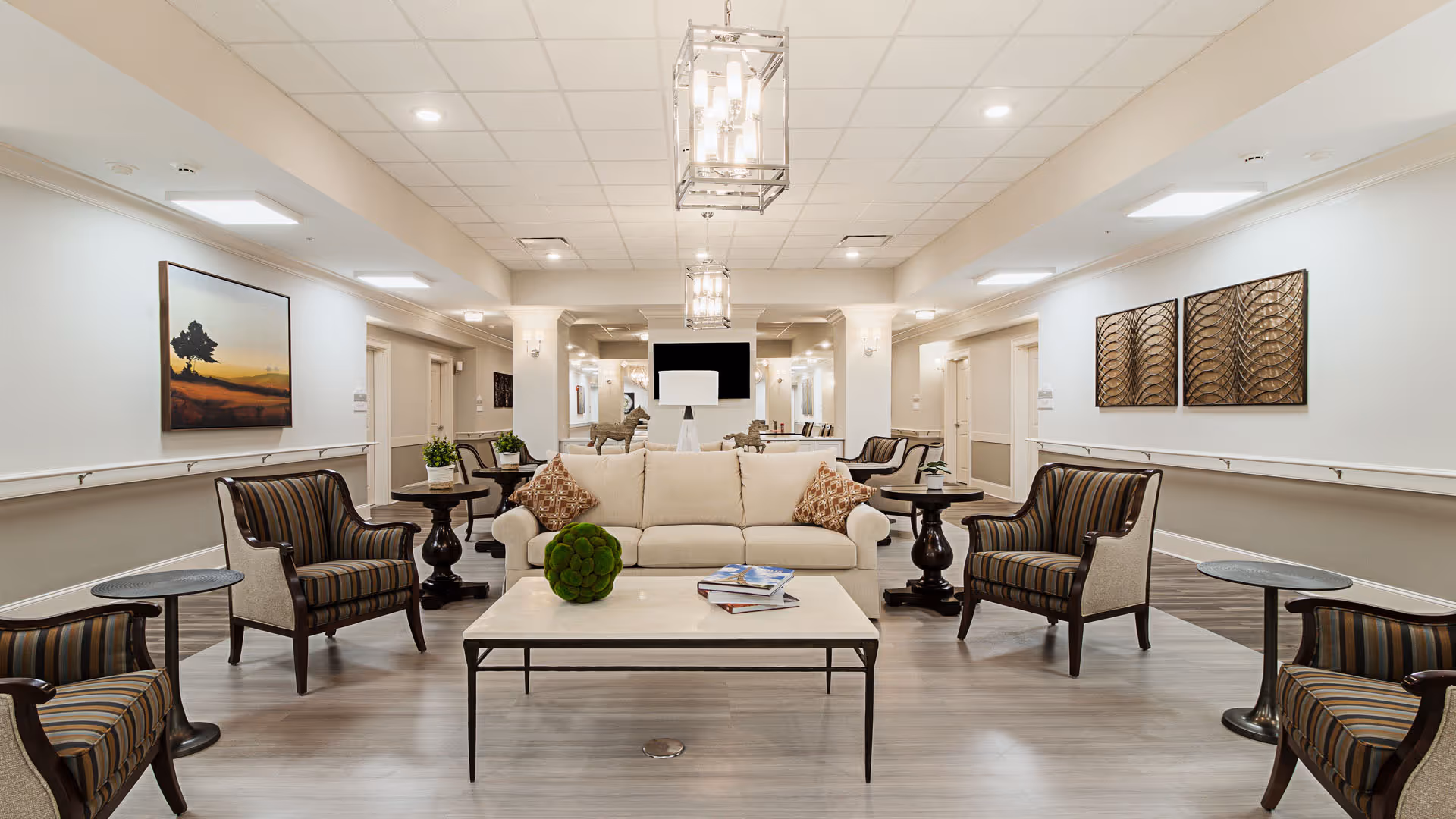 Spacious senior living lounge with a central sofa, armchairs, coffee table, and wall art.