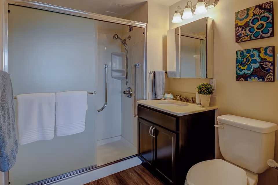 Small bathroom with a sliding glass shower, dark wood vanity with sink and mirror, and a toilet.